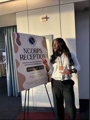 A woman stands next to a sign for the NCOBPS Reception, indicating it will be held on March 14, 2024, with event details and a note about refreshments and networking opportunities.