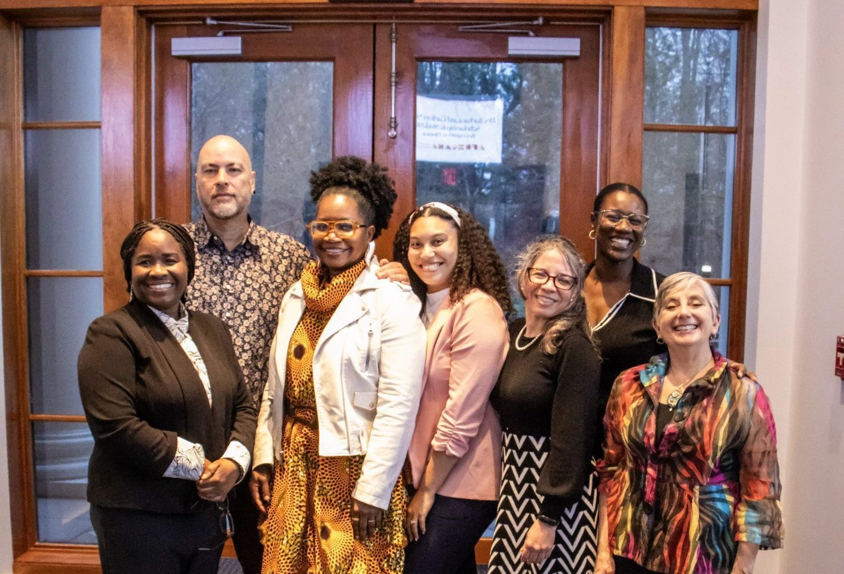 ASI Staff  at the Molette Dinner 2025: A group of seven people stand smiling in a warmly lit room with large windows. They are dressed in professional and colorful attire.